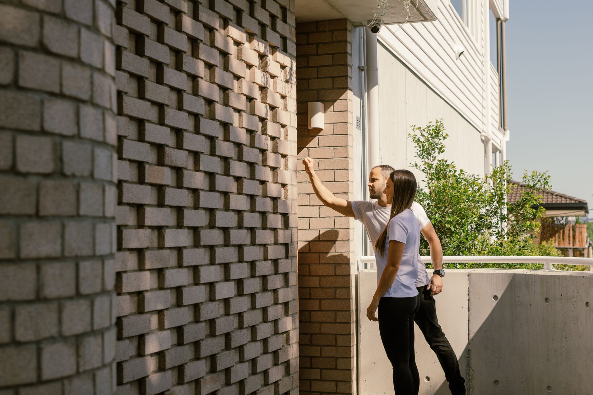 Couple standing outside a building, pointing at a brick wall as they inspect it.